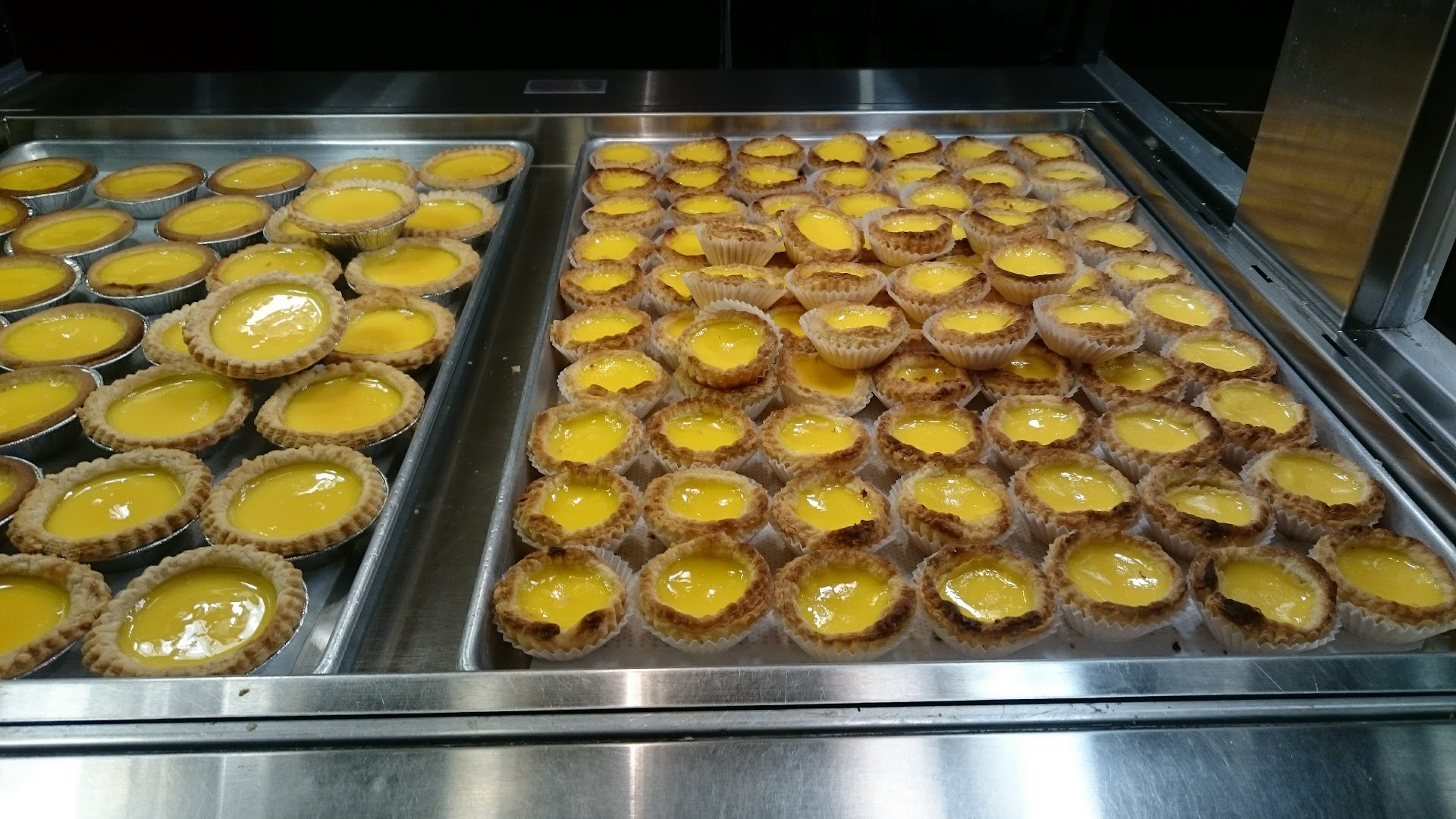 Rows of freshly baked egg tarts in metal trays